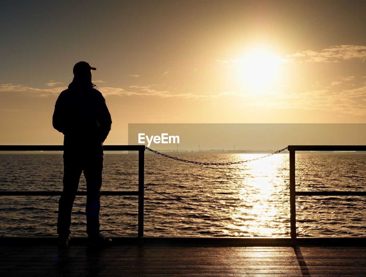 Adult tall man on pier board look over sea to morning sun. smooth water in bay. vignetting effect.