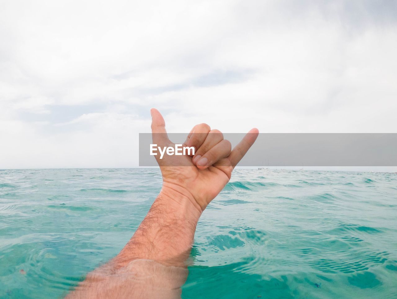 CLOSE-UP OF HAND AGAINST SEA