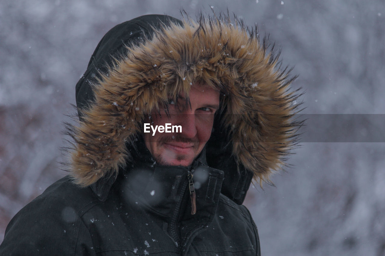 Portrait of man wearing fur coat standing outdoors during snowfall