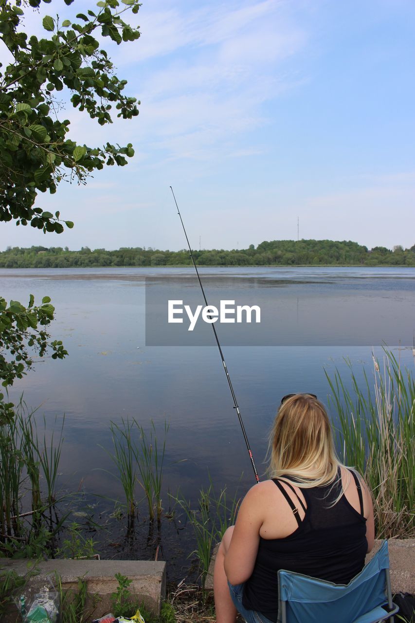 Rear view of woman fishing in lake against sky