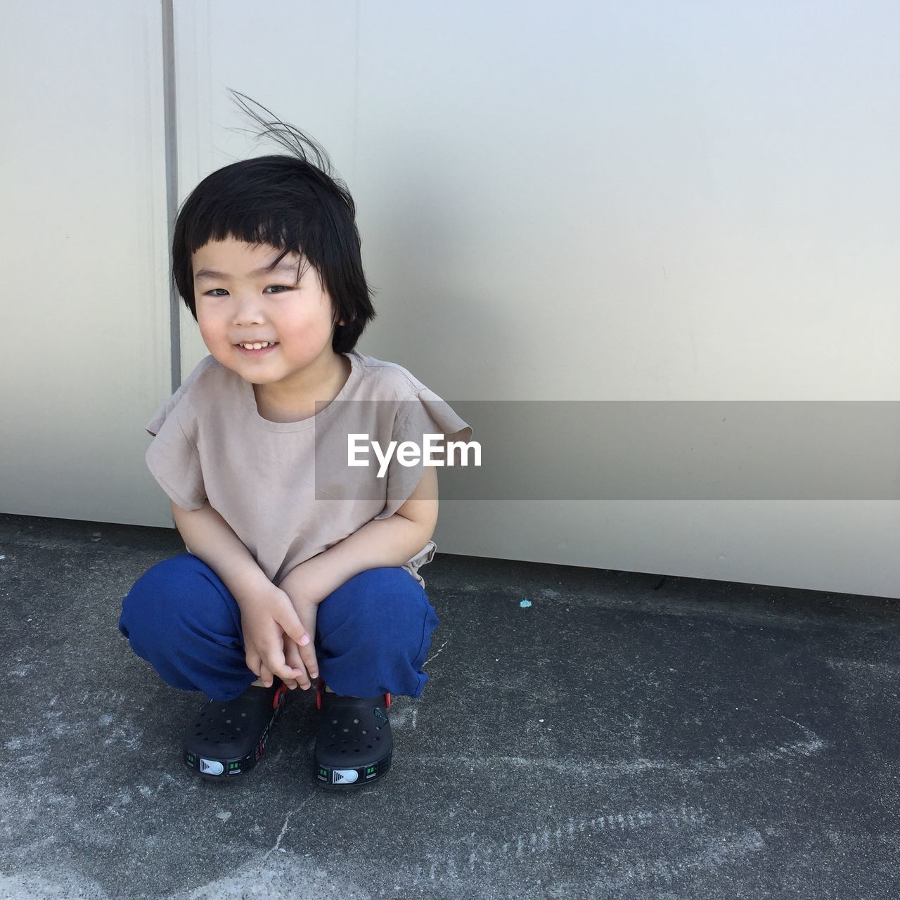 Portrait of smiling cute boy crouching on road against wall