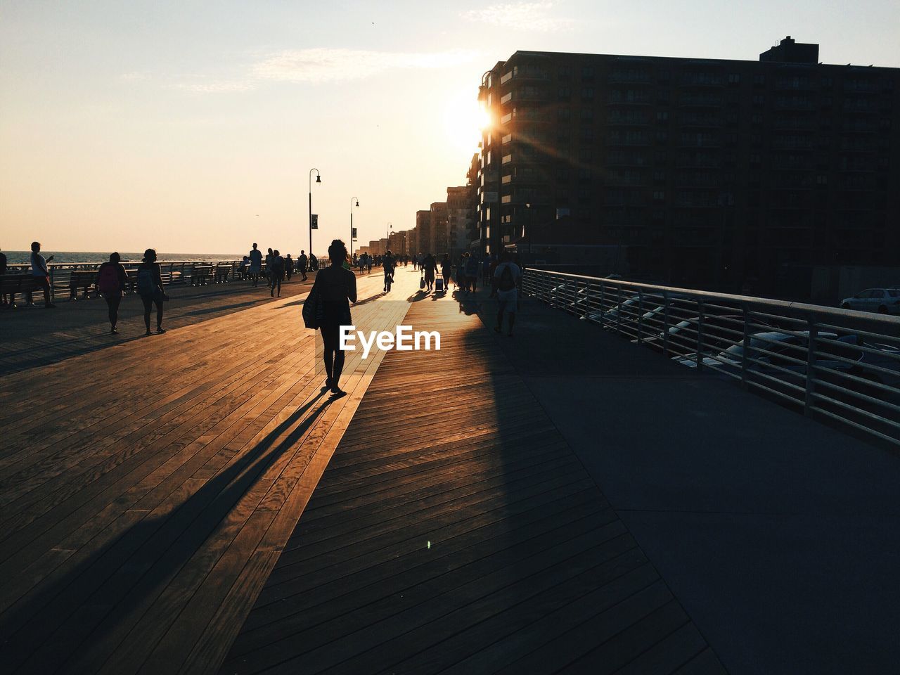 Silhouette people walking on bridge in city during sunset