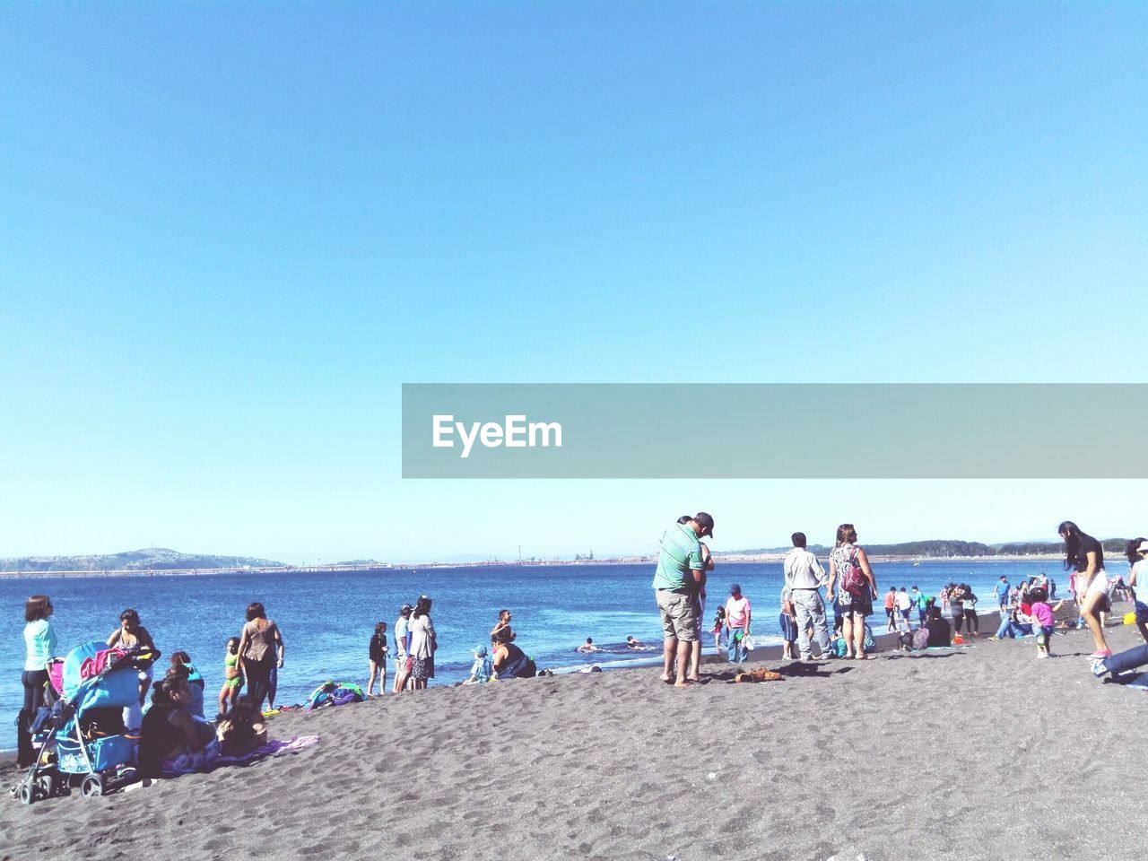 People enjoying at beach against clear blue sky