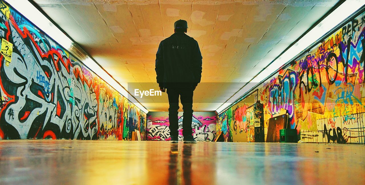 Rear view of man standing amidst colorful walls with graffiti