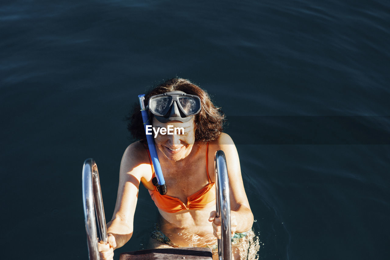 High angle view of happy woman climbing ladder of boat on sea