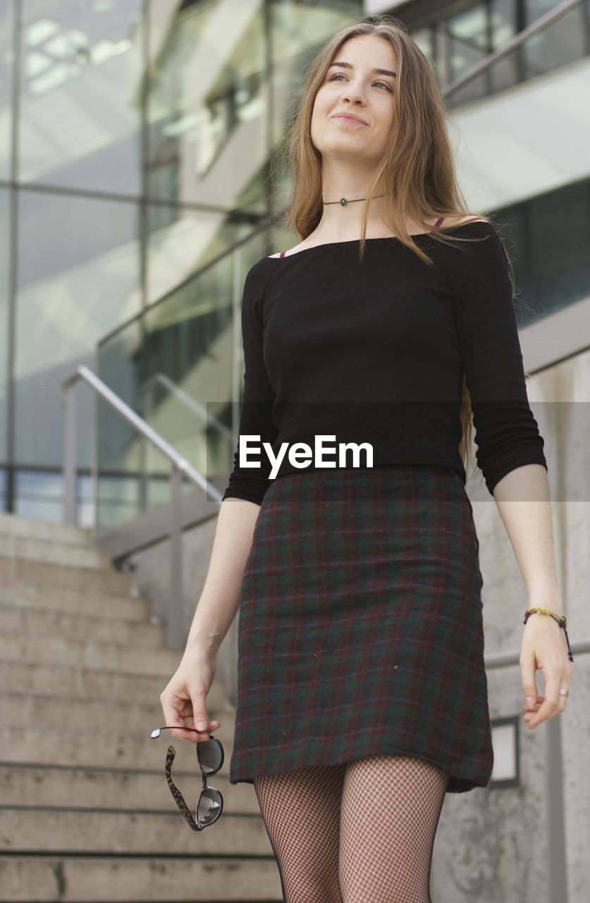 Young woman looking away while standing against building