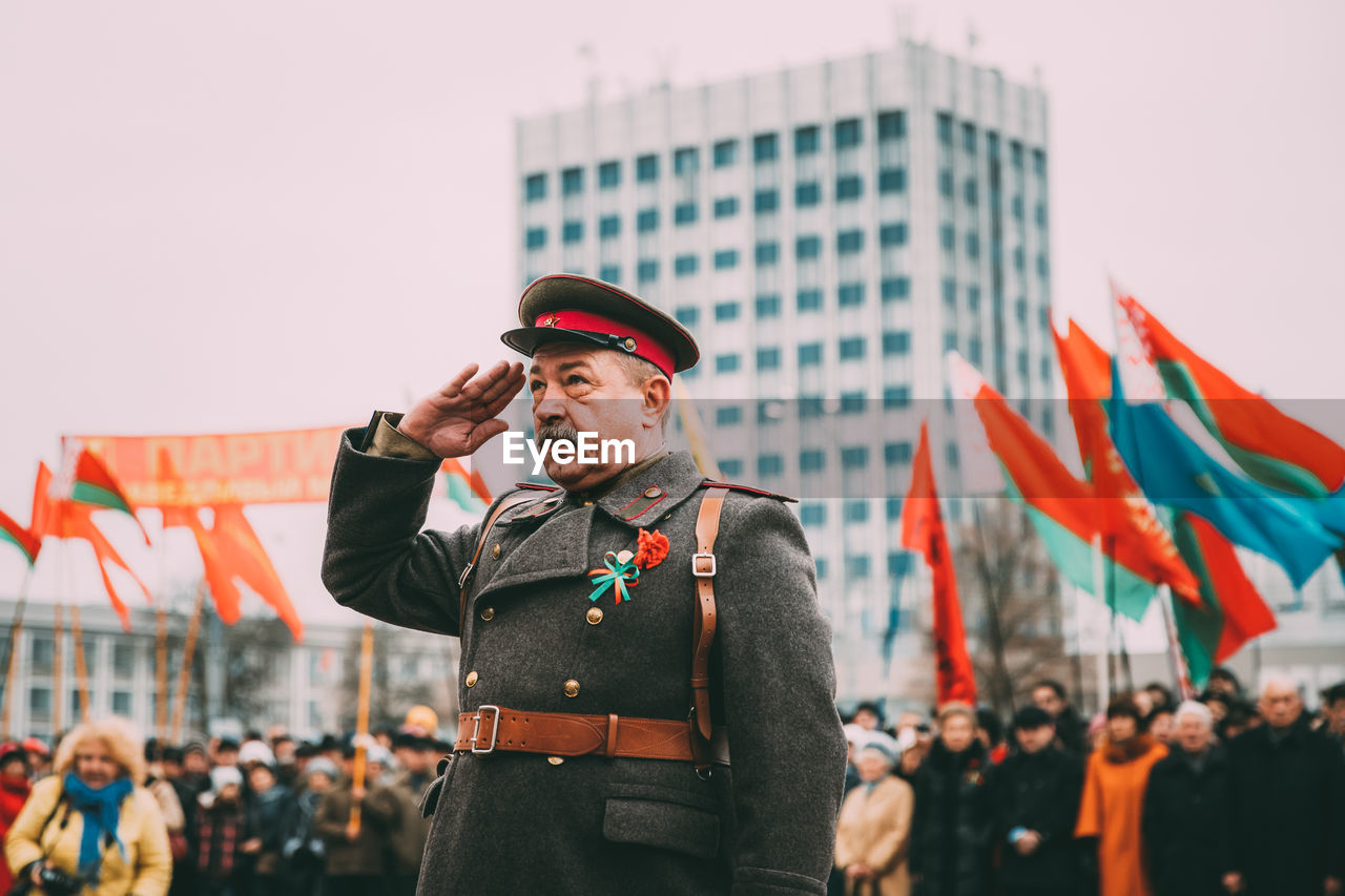 MIDSECTION OF MAN STANDING IN FRONT OF FLAGS