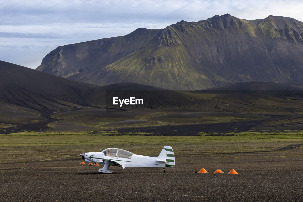 White monoplane parked on spacious grassy valley surrounded by rough picturesque mountain range in nordic nature