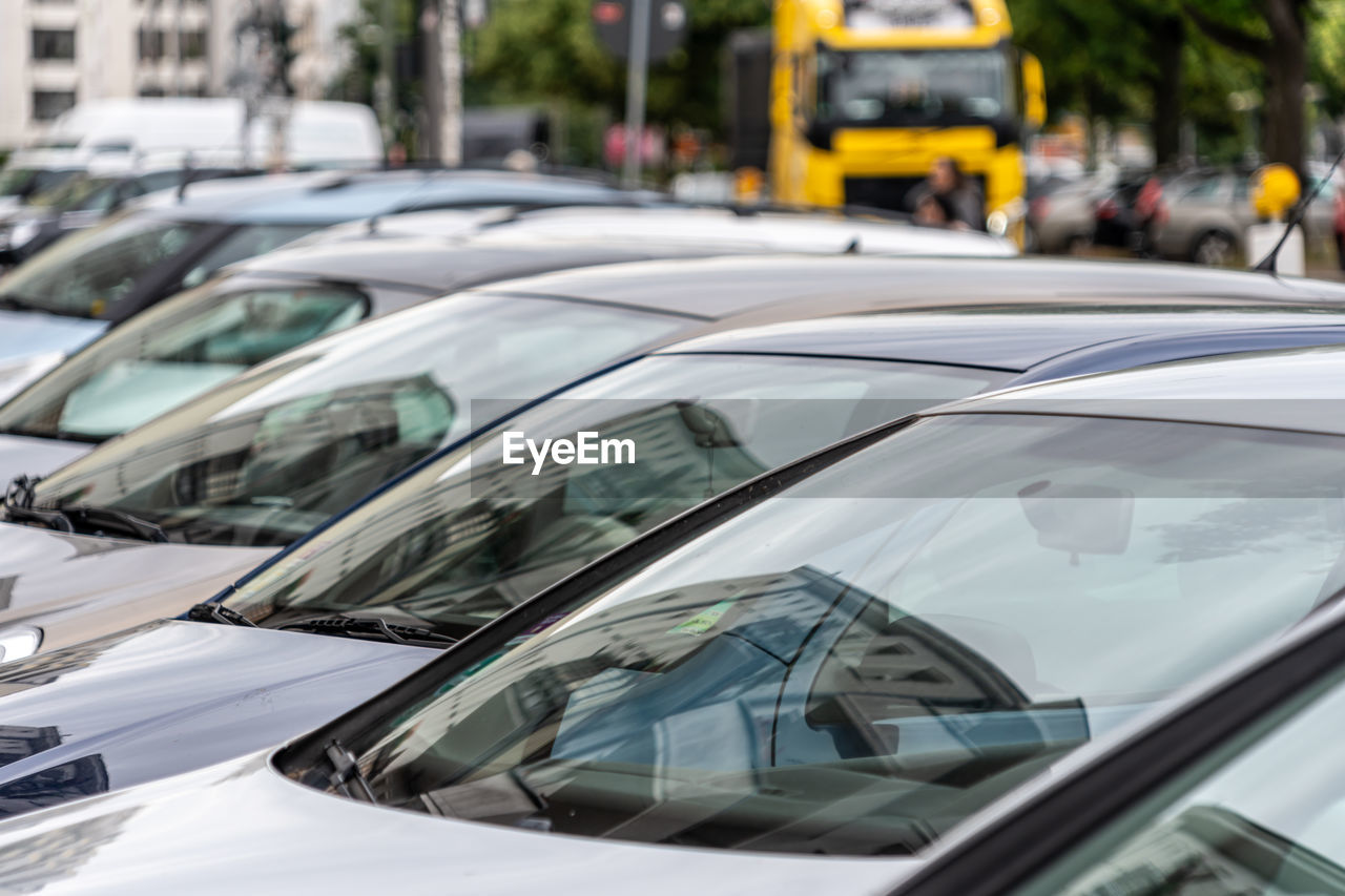 car, motor vehicle, mode of transportation, transportation, vehicle, land vehicle, traffic, city, street, automobile, glass, in a row, road, taxi, architecture, city street, city life, consumerism, wheel, luxury vehicle, windshield, retail, supercar, focus on foreground, business, traffic jam, outdoors, no people, sports car, day, close-up, car dealership, reflection