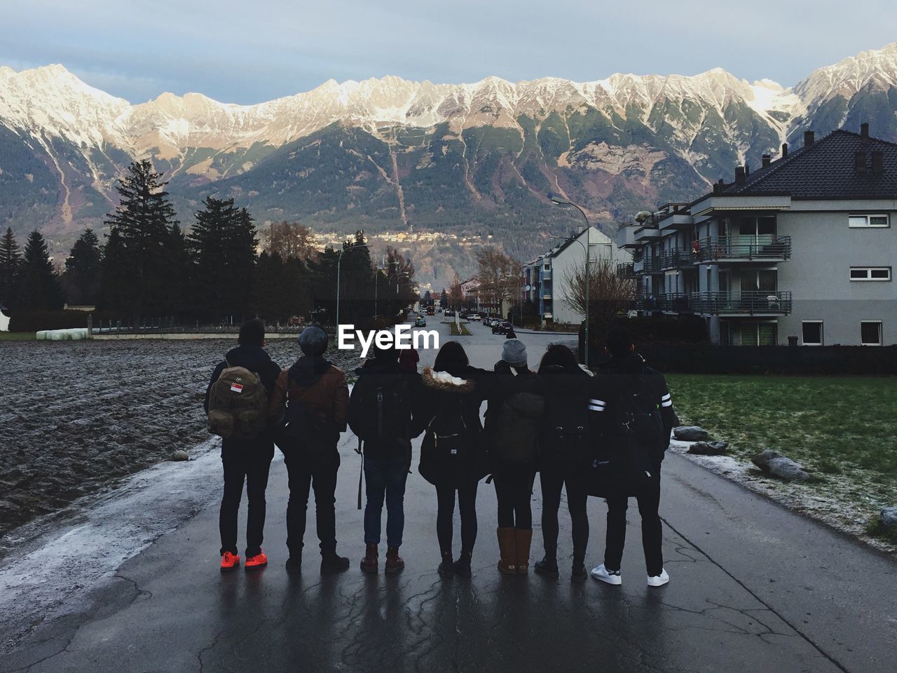 Full length rear view of friends standing on wet road against mountains