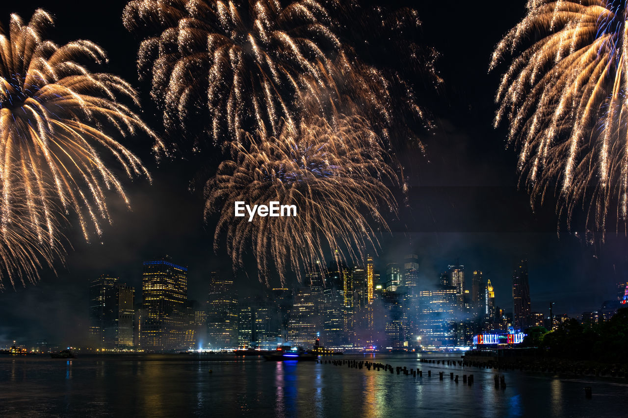 FIREWORK DISPLAY OVER RIVER BY BUILDINGS AGAINST SKY