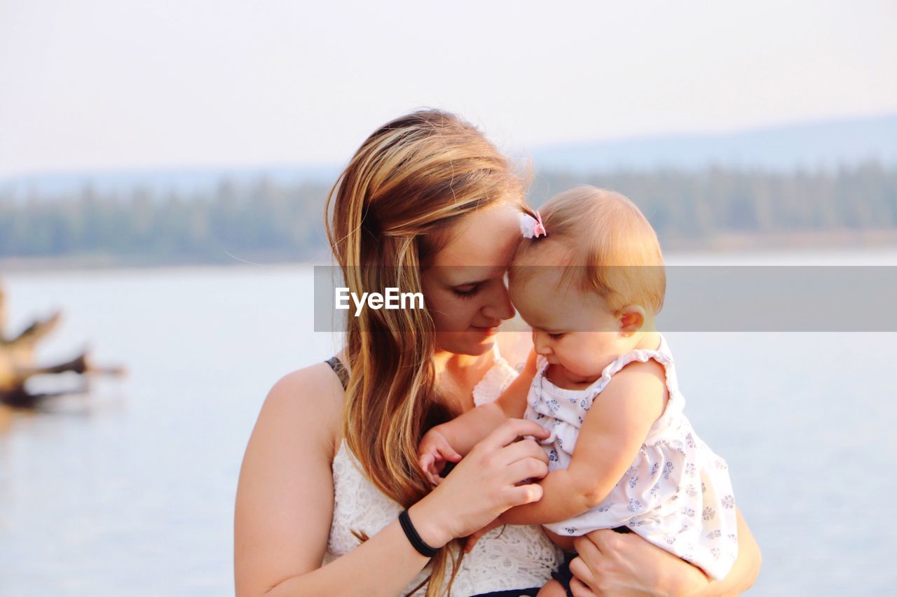 Close-up of mother holding baby girl against sea