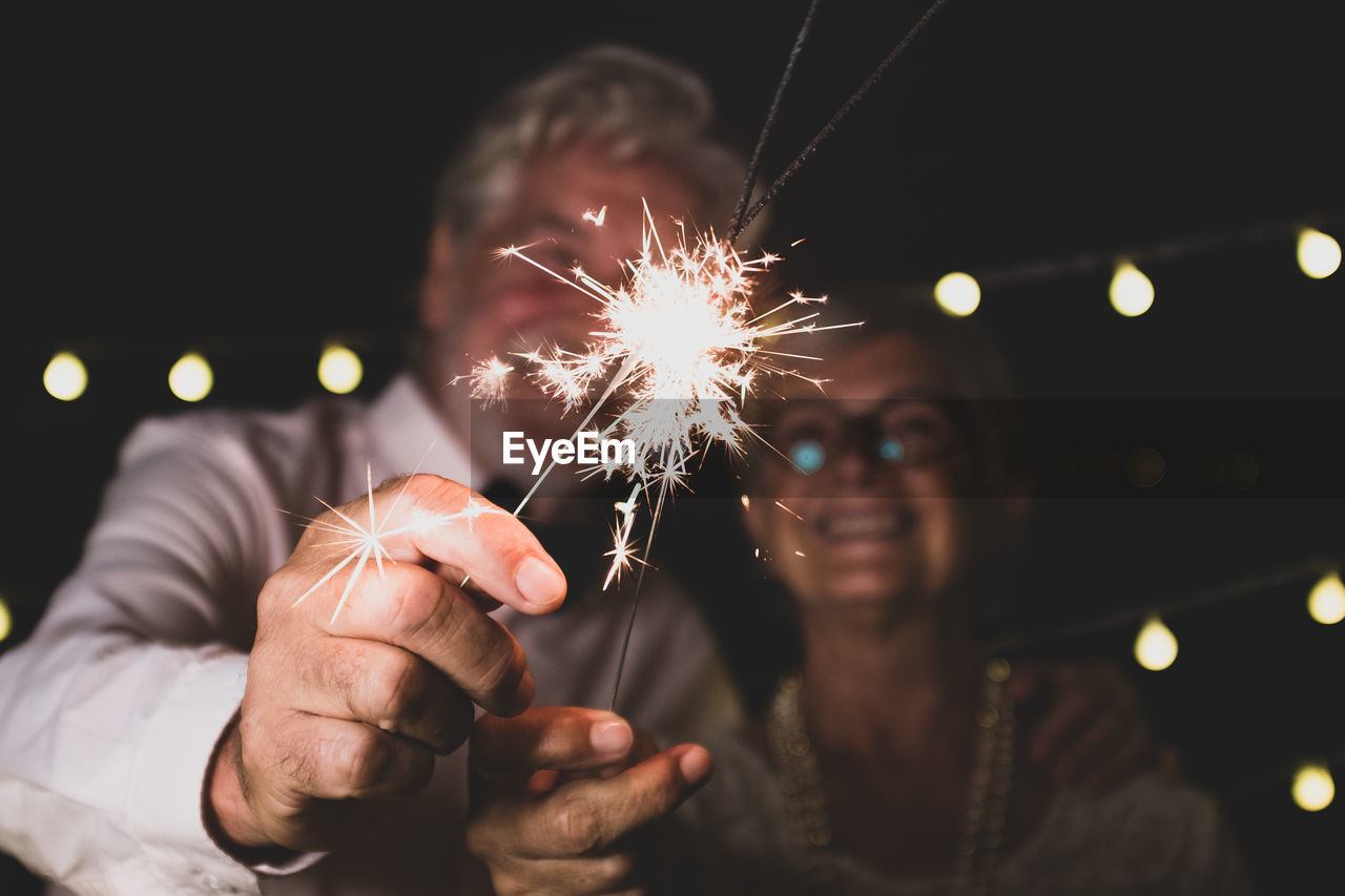 Senior couple holding sparklers standing outdoors at night