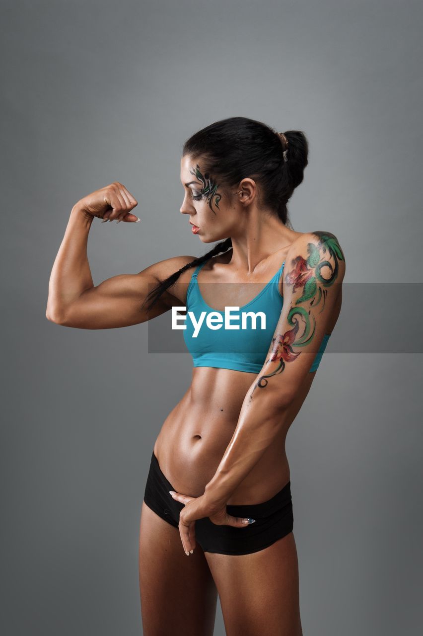Muscular woman flexing muscles while standing against gray background