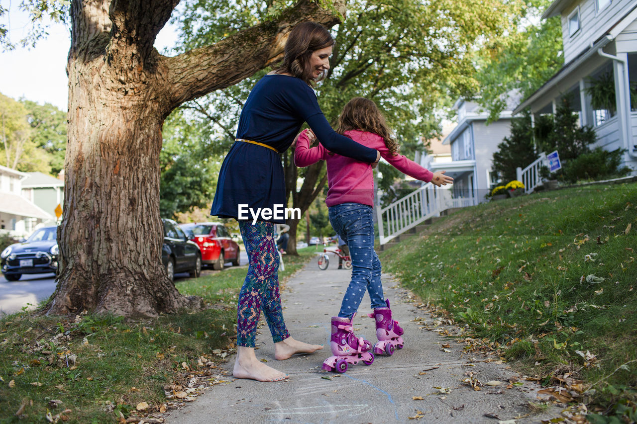 Mother assisting daughter in skating on footpath during autumn