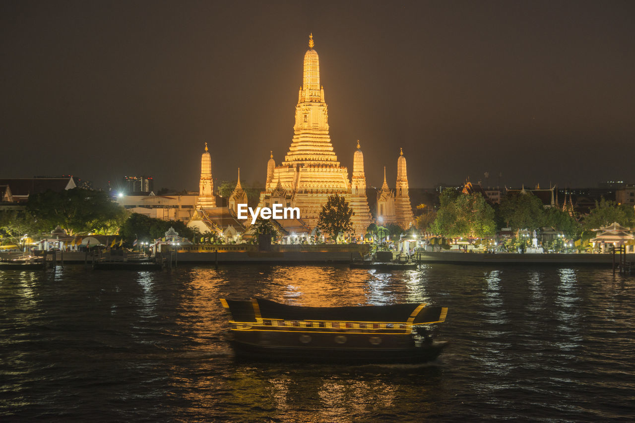 ILLUMINATED TEMPLE BUILDING BY RIVER AGAINST SKY IN CITY