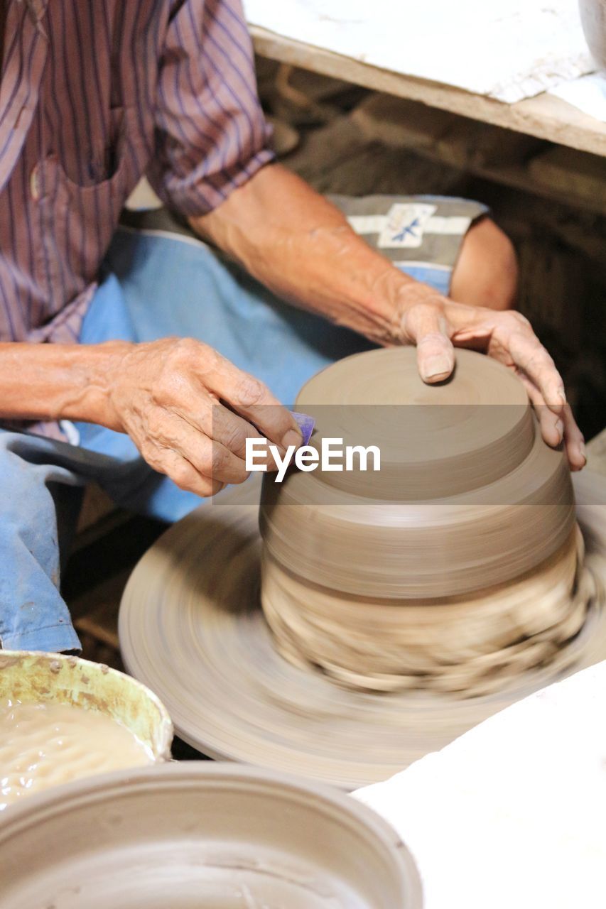 Midsection of man molding shape on pottery wheel
