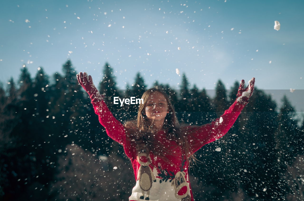 Smiling girl throwing snow while standing outdoors