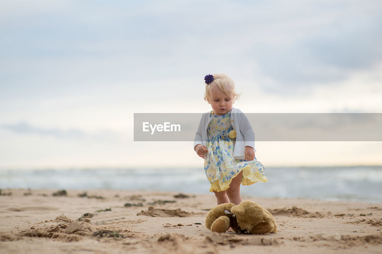 Girl with stuffed toy at beach against sky