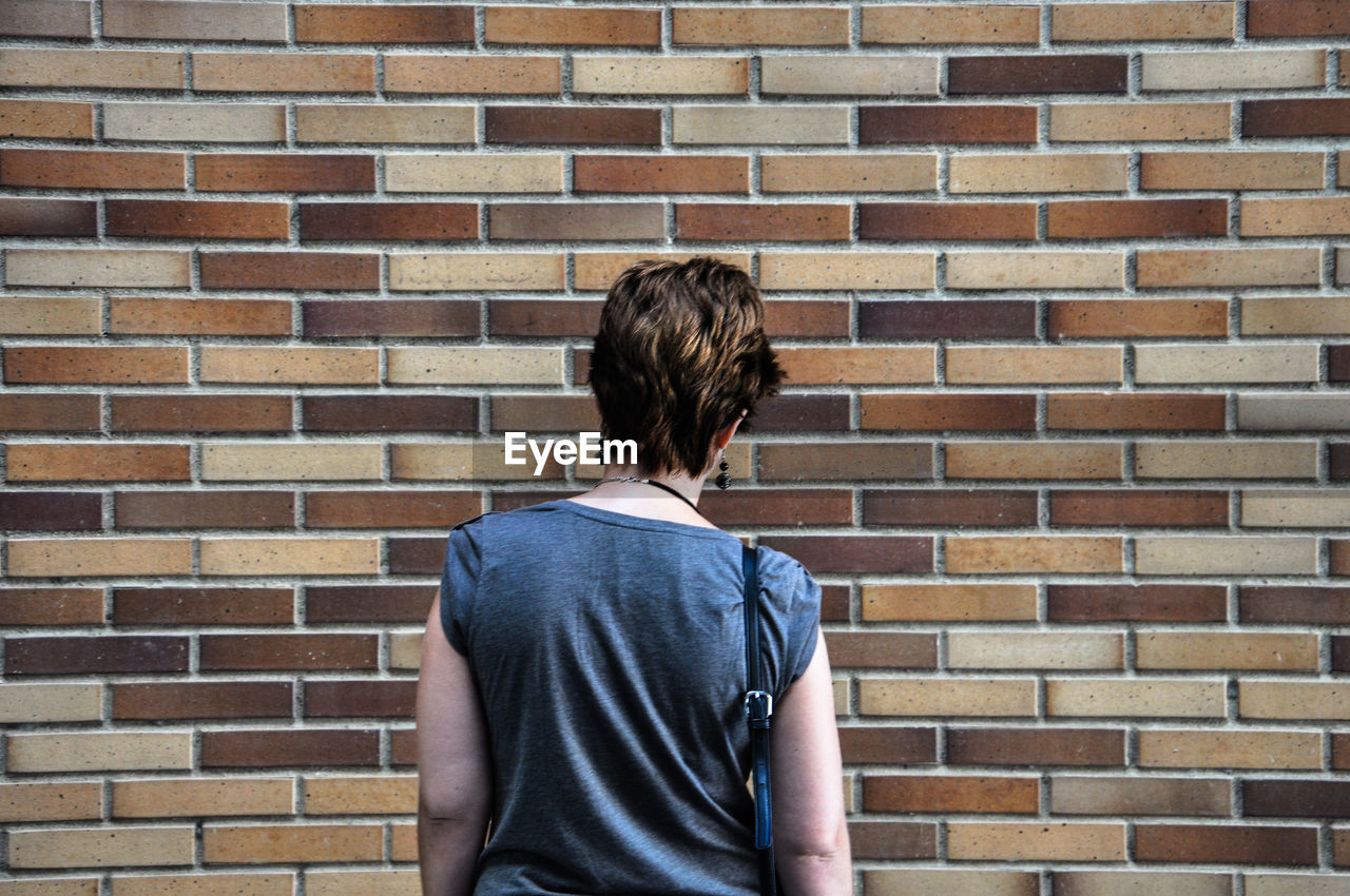 Rear view of woman standing against brick wall