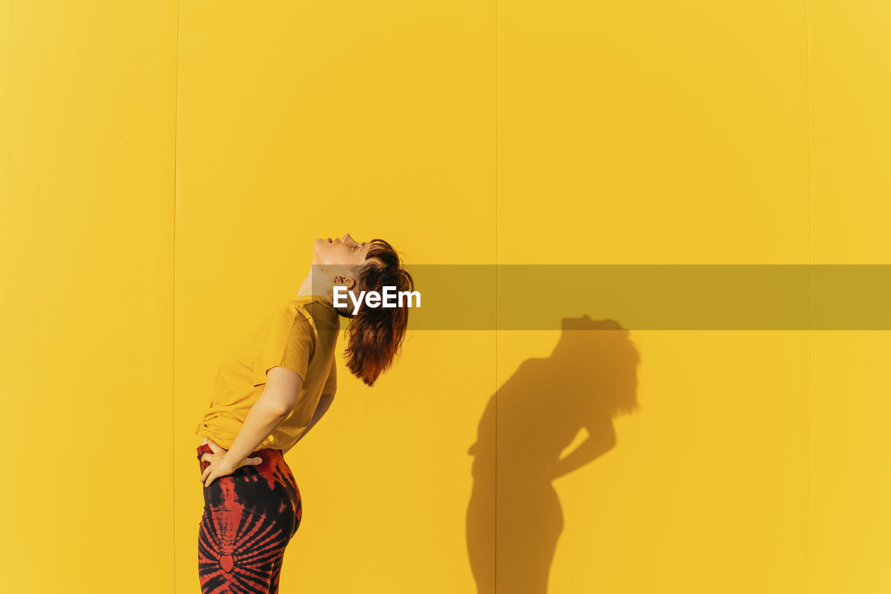 Woman with hand on hip standing by wall during sunny day