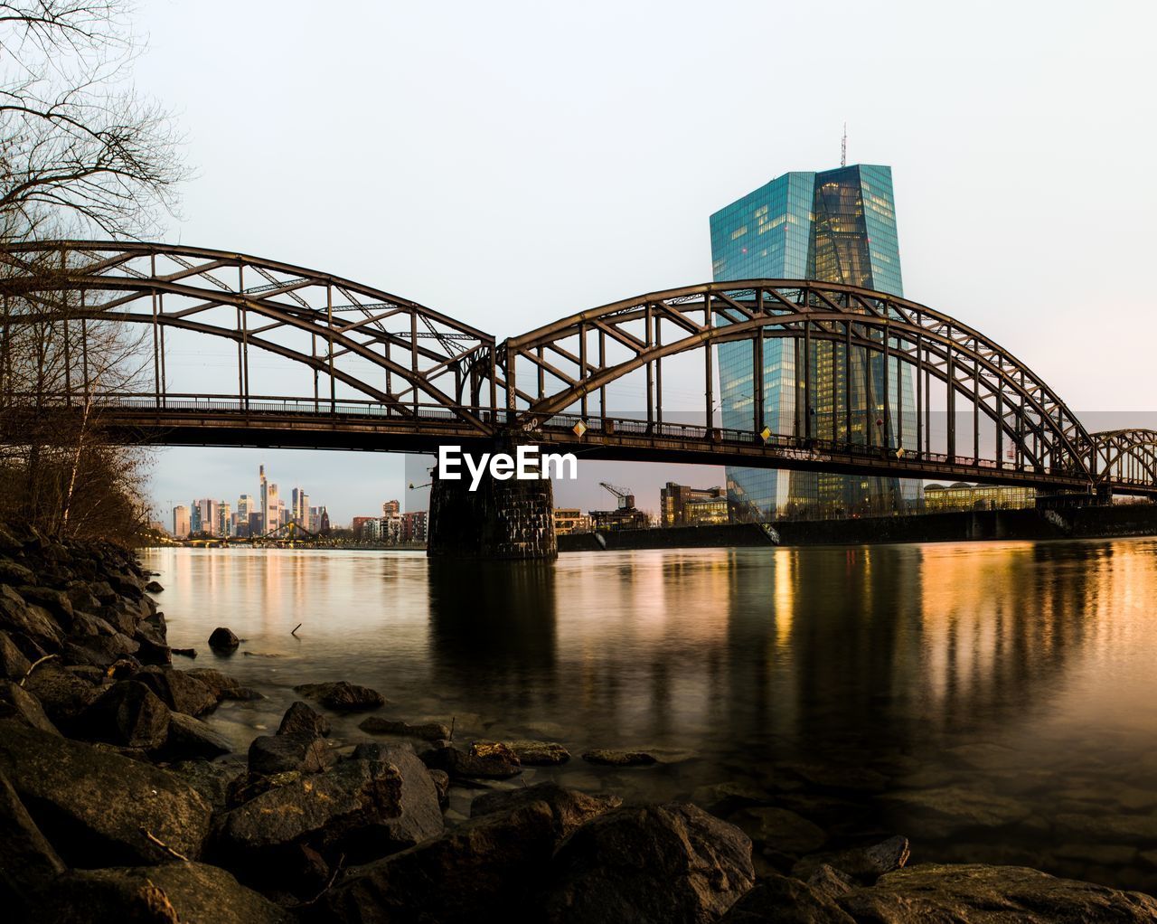 Arch bridge over river against clear sky in city during sunset