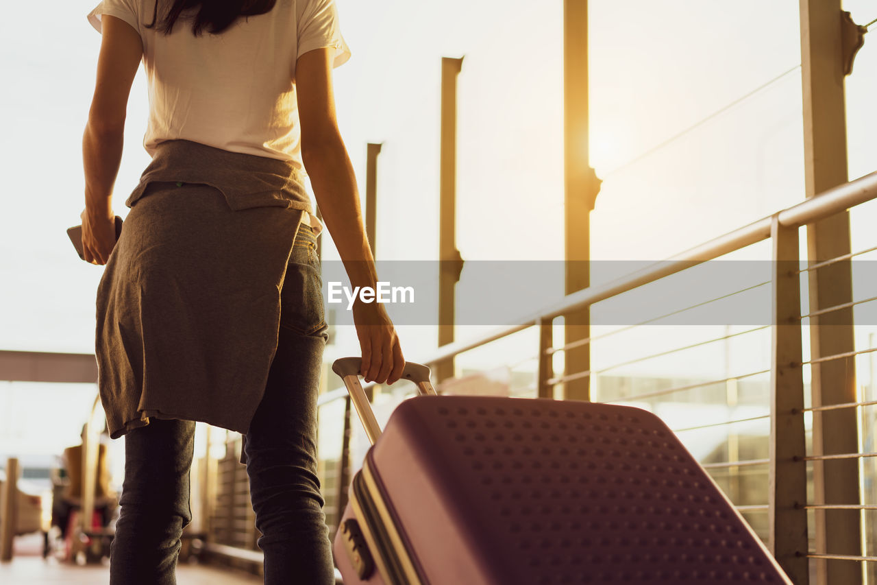 Midsection of young woman holding luggage at airport