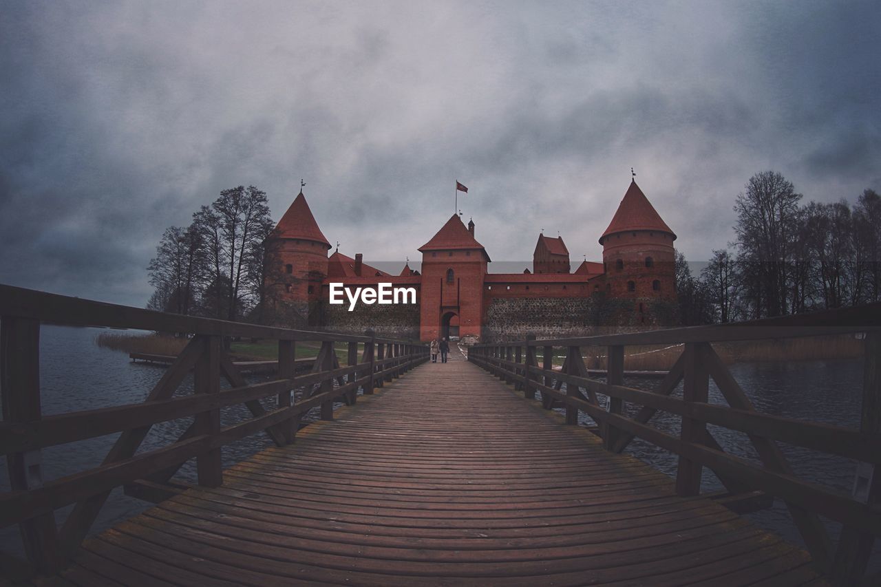 Boardwalk leading castle against cloudy sky