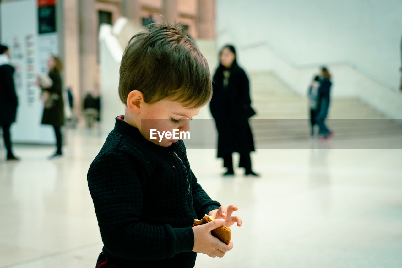 Side view of boy holding food while standing in city