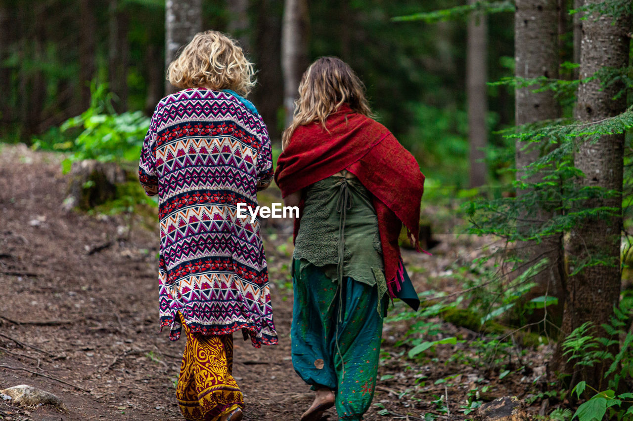 REAR VIEW OF TWO WOMEN WALKING IN THE FOREST
