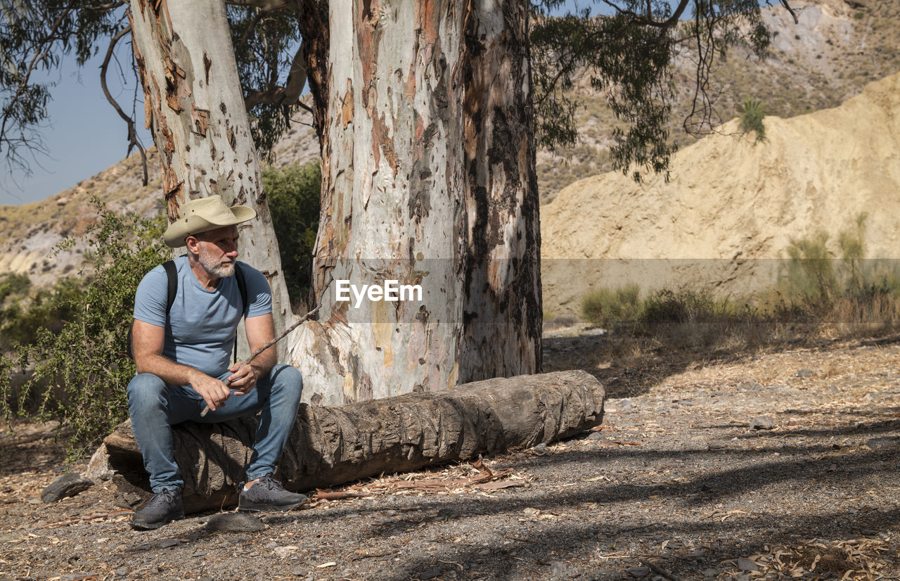 Portrait of adult man in cowboy hat and jean sitting in a rural area