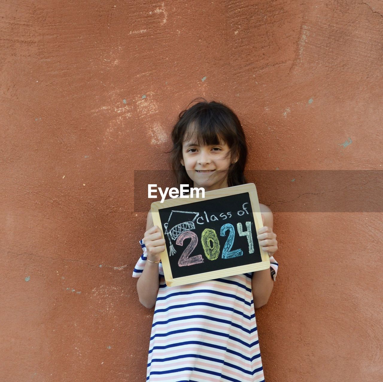 Portrait of smiling girl with message standing against brick wall