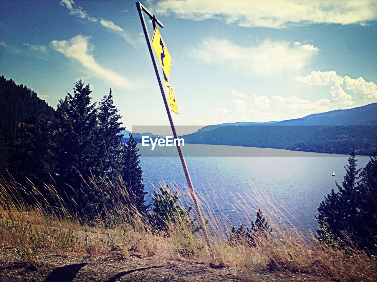 Road sign in front of lake against sky