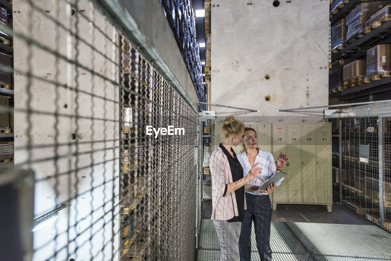 Women using laptop in high rack warehouse