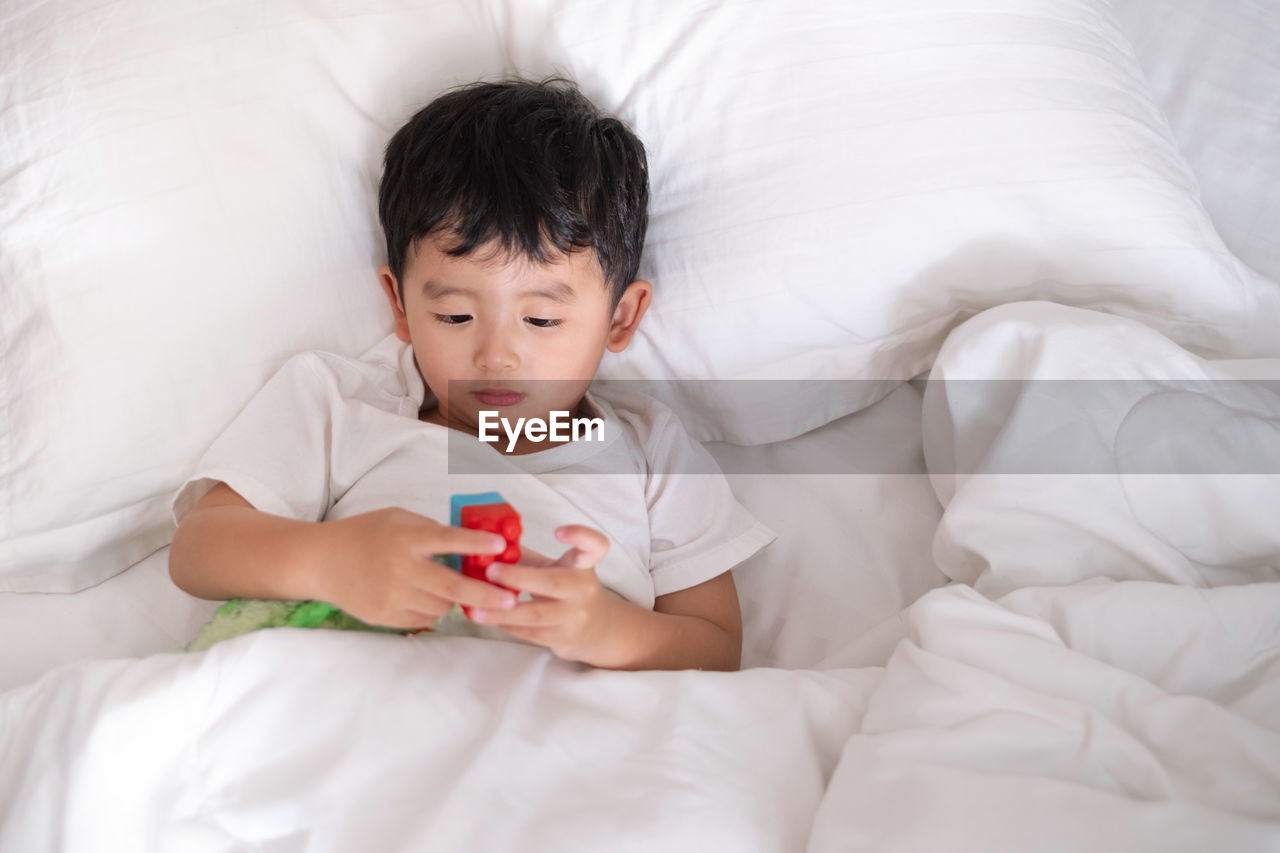 High angle view of cute boy playing with toy while lying on bed at home