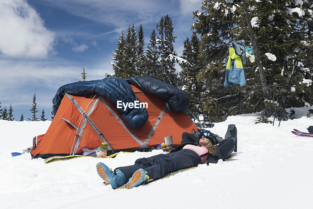 Young woman relaxing by tent on snow covered mountain