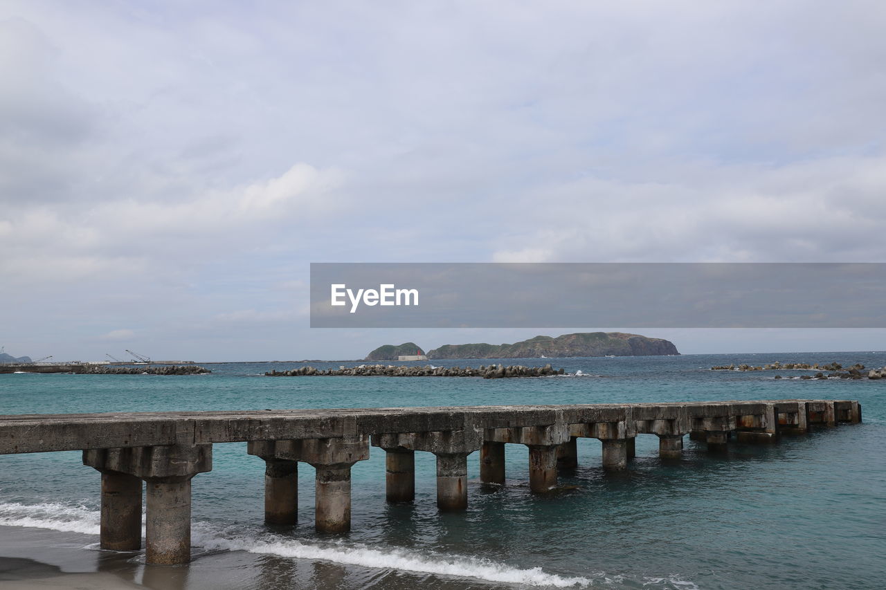 WOODEN POSTS ON PIER OVER SEA AGAINST SKY