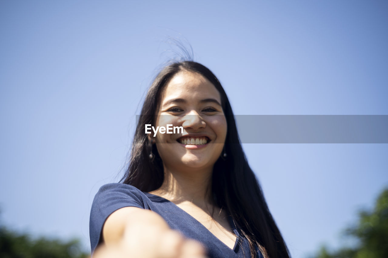 Low angle portrait of smiling young woman against clear blue sky