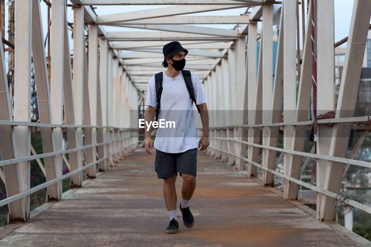 Young millennial walking on footbridge while wearing a protective mask to prevent covid-19 infection