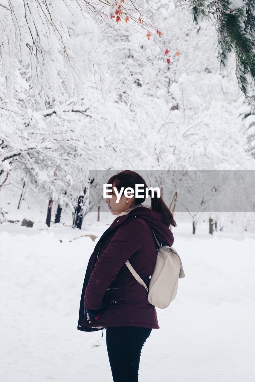 Side view of young woman standing in forest during winter