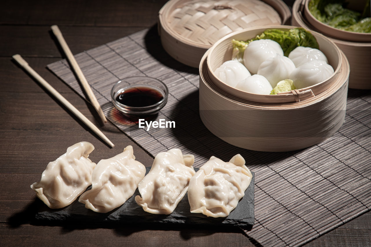 Dim sum in bamboo steamer and gyozas with soya sauce on dark background.