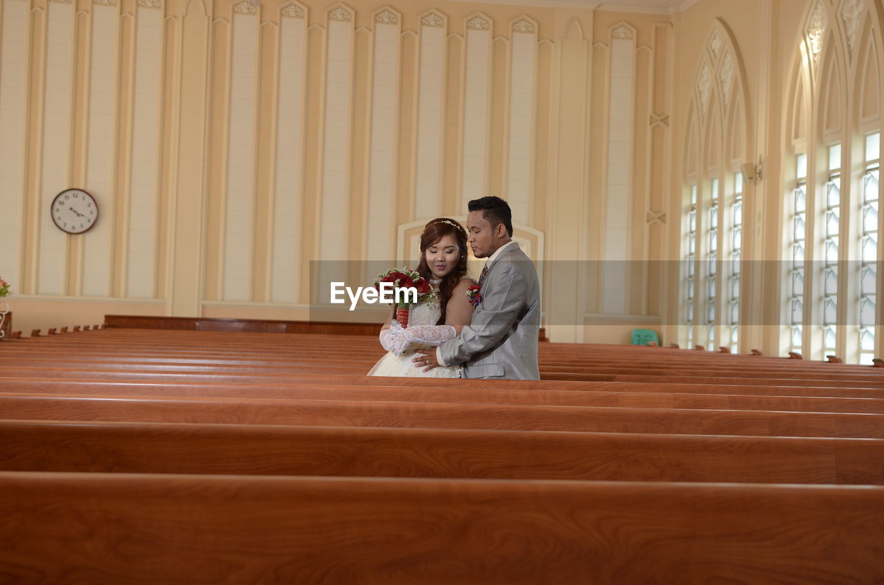 Bride and groom standing amidst benches in church