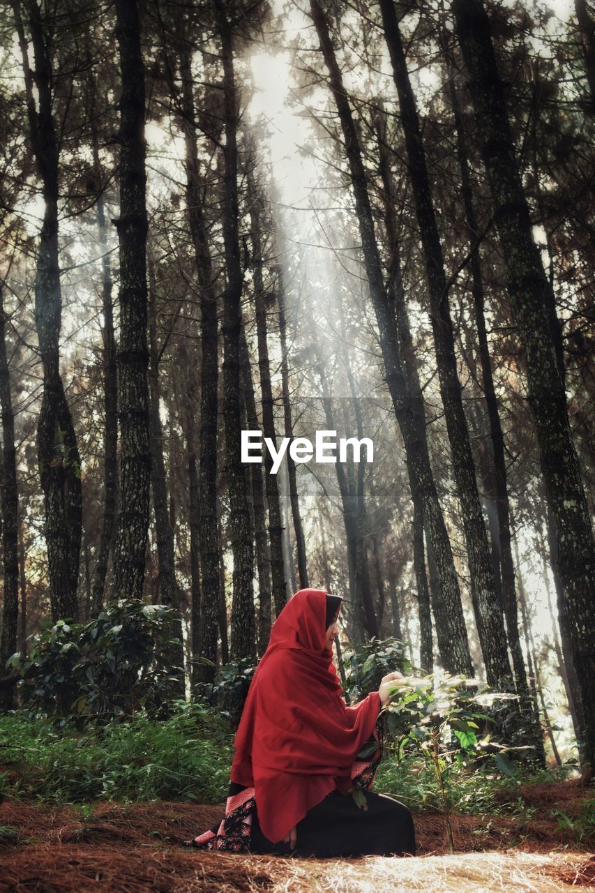 Woman sitting against trees in forest