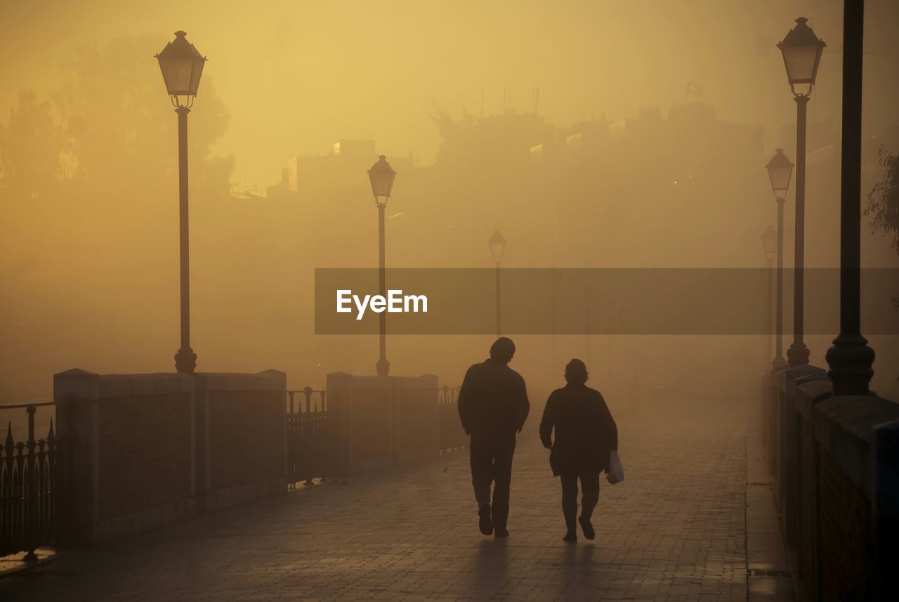 REAR VIEW OF PEOPLE WALKING ON STREET LIGHT