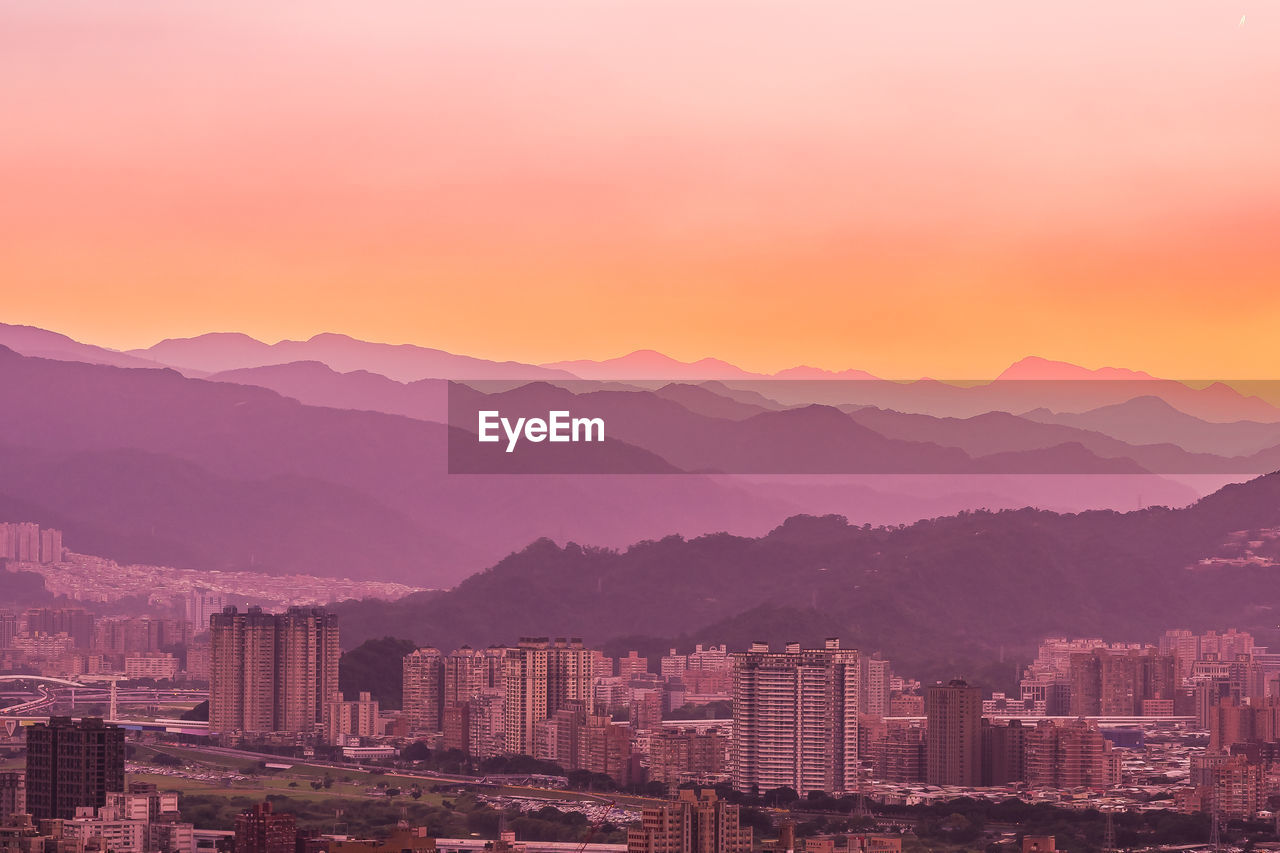 Aerial view of city by mountains against orange sky