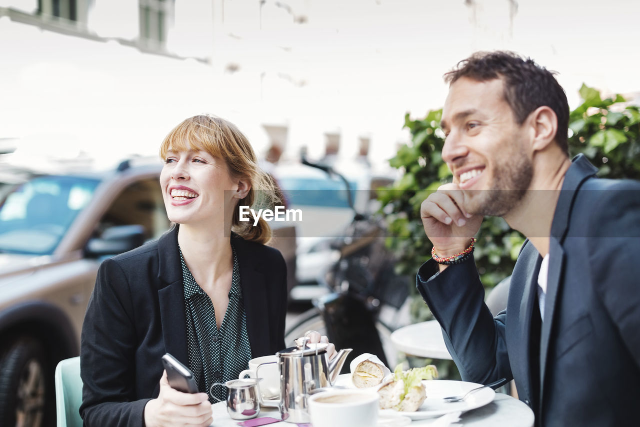 Happy business commuters looking away while sitting at sidewalk cafe