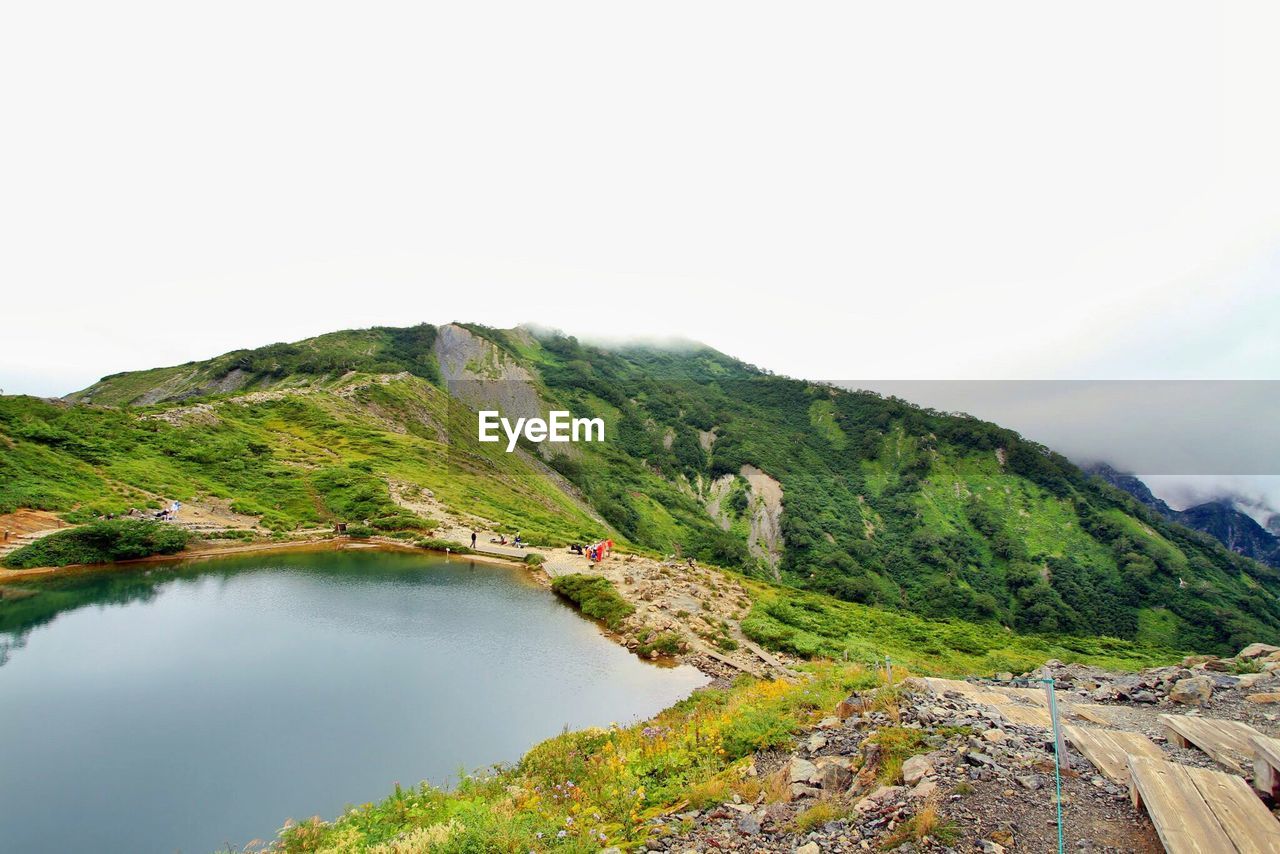 Scenic view of green mountain by lake against sky