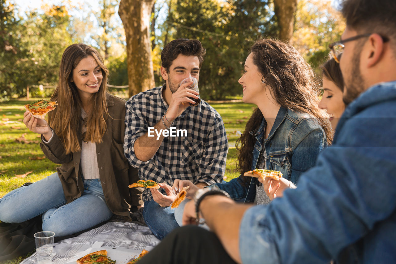 Smiling friends eating food in picnic at park