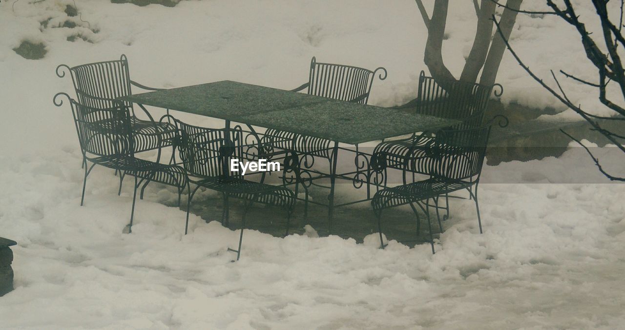 Empty chairs and table on snow covered field