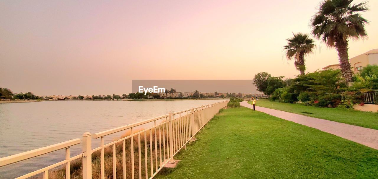 water, sky, plant, palm tree, tree, tropical climate, nature, sunset, beauty in nature, grass, travel destinations, architecture, scenics - nature, sea, tranquility, travel, environment, land, landscape, footpath, walkway, tranquil scene, beach, tourism, vacation, holiday, built structure, trip, outdoors, summer, no people, idyllic, clear sky, sunlight, green, sun, relaxation, tropical tree, city, twilight, coconut palm tree